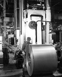 Black & white photo of workers rolling steel