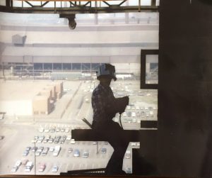 A color photograph shows a man in silhouette high above the ground wearing protective workclothes.