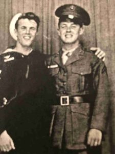 A black-and-white photo shows two brothers, in military uniforms, smiling and embracing.