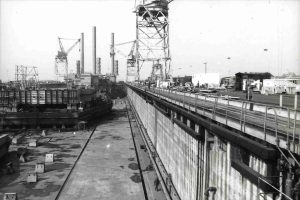 A black and white photo shows oil rigs under construction at the shipyard's building basin