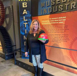 A woman stands in the BMI's lobby holding a red and green hard hat.