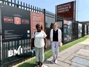Two women stand beside an outdoor exhibition along the museum's Key Highway fence