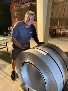 A man stands behind a hip-height coil of rolled steel